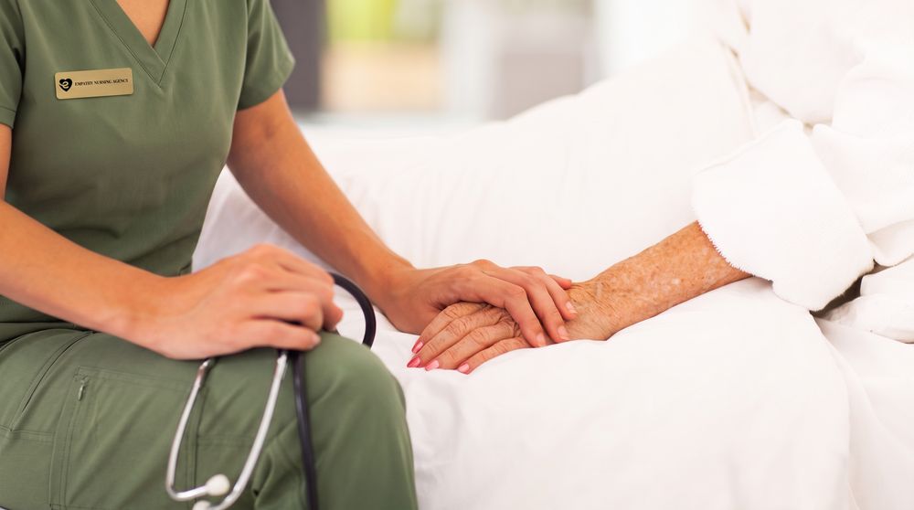 A nurse holding a client's hand at the bedside