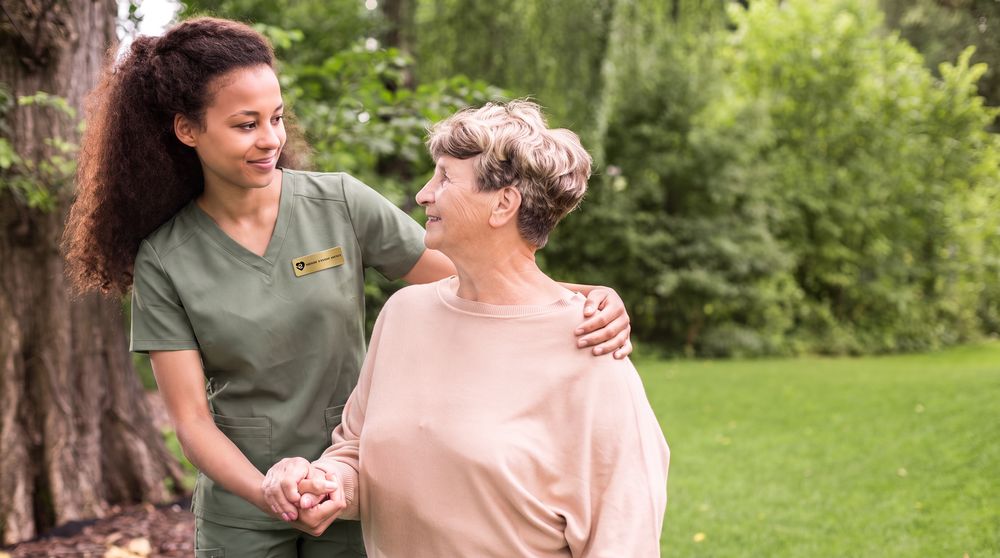 A caregiver walking arm in arm with a client through a park